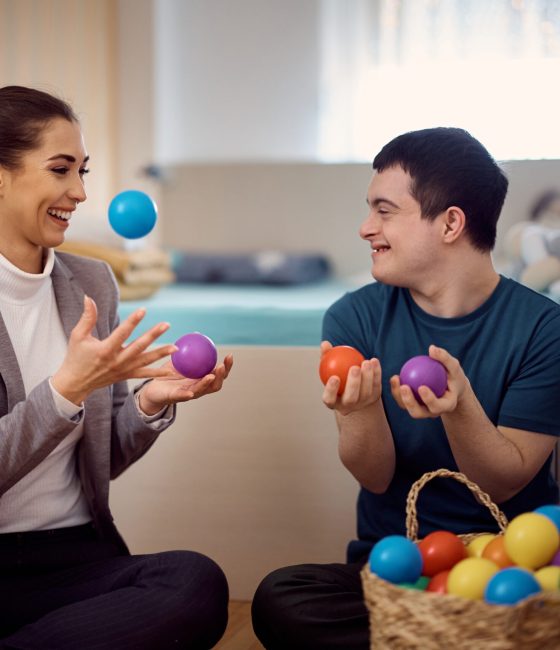Happy psychologist and man with down syndrome having fun while playing with plastic balls during home visit.